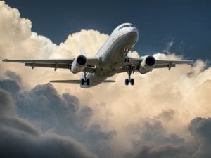 Bildet viser et fly som flyr. Bakgrunnen er blå himmel, og skyer.