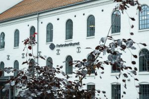 Bildet viser en hvit murvegg med Forbrukertilsynets logo
