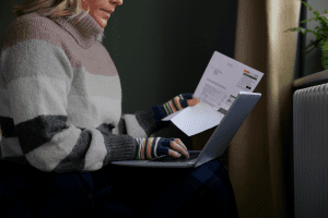 Dame som sitter ved vindu og betaler papirfaktura på en pc